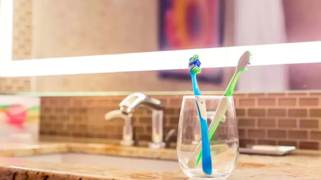 Escovas de dentes dentro de copo em cima de pia de banheiro